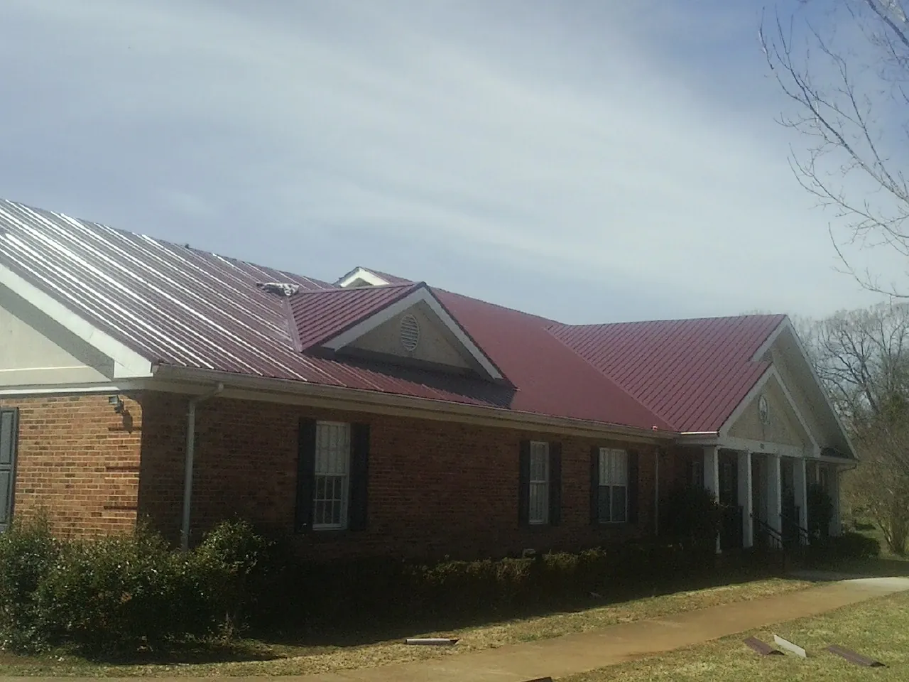 Red metal roof with gabled entries on a long brick building, from a Hail Damage Roof Repair job in Harmon