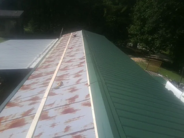 Old rusted panels beside newly installed green metal roofing — Wind Damage Roof Repair by Roofing Brothers in Harmon