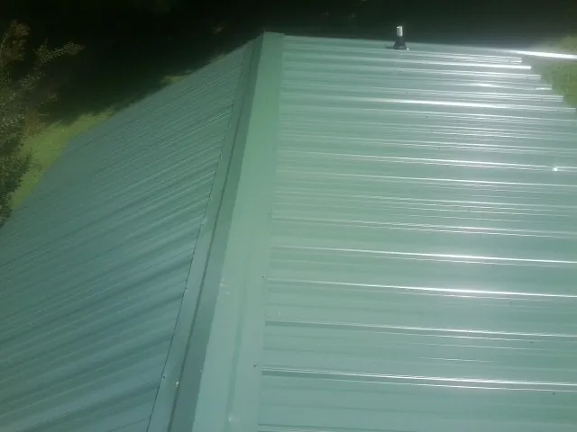 New green metal panels meeting at the ridge of a roof — Flat Roof Repair work by our crew in Harmon