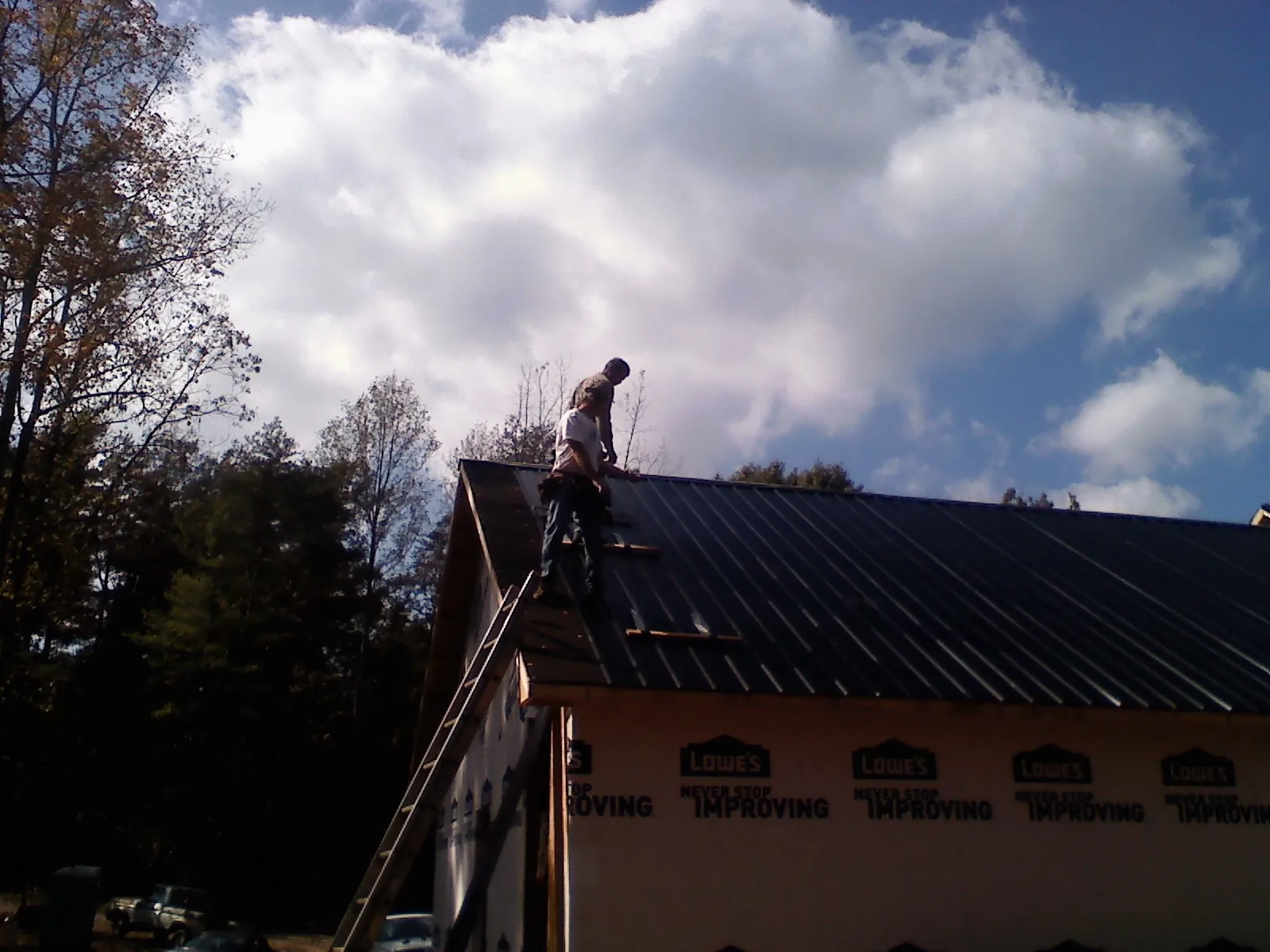 Roofer fastening dark metal panels high against a cloudy sky, from a Roof Inspection job in Harmon