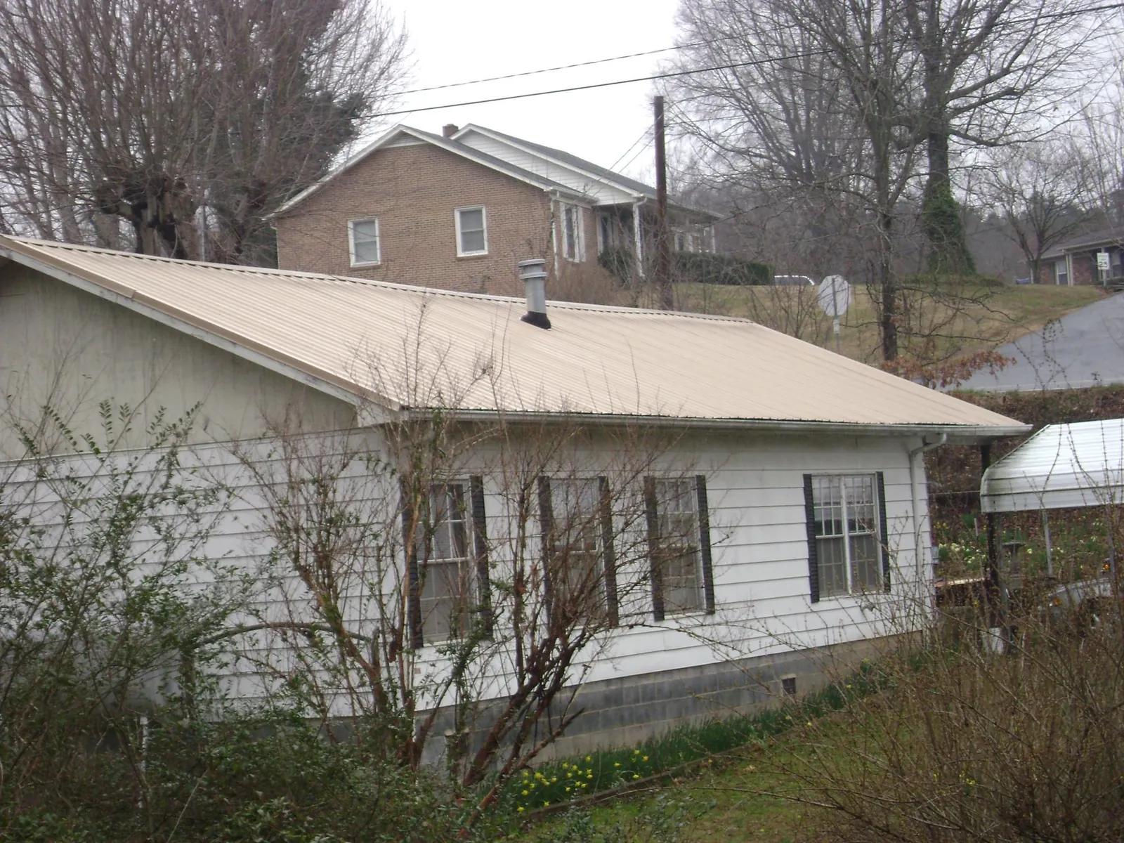 Tan metal roof on a white sided house set into a hillside — Commercial Roofing by Roofing Brothers in Harmon