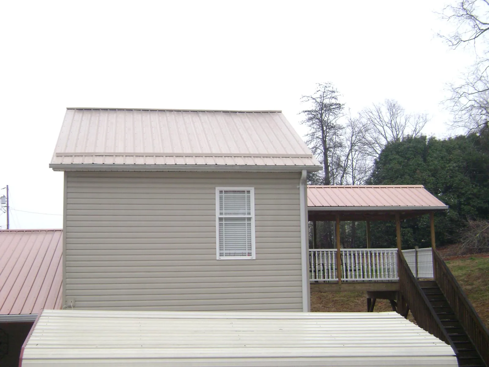 Tan metal roofs on a two story addition and attached porch, from a Roof Replacement job in Harmon